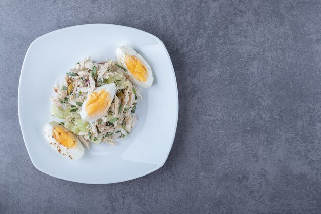 Plaat van salade met gekookt ei op stenen tafel.