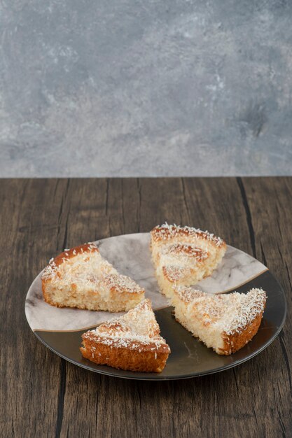 Plaat van smakelijke cakeplakken met kokos hagelslag op houten tafel.