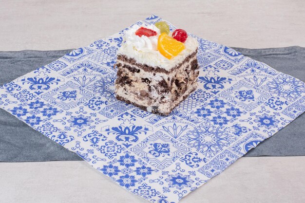 Plak van witte cake met fruitplakken op tafelkleed.