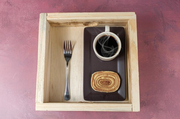 Plakje bolo de rolo naast kopje koffie en een vork over een houten dienblad.