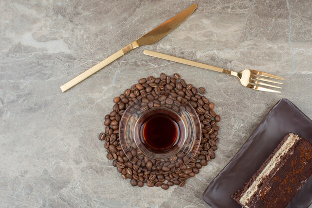 Plakje chocoladetaart, koffiebonen en glas thee op marmeren tafel.