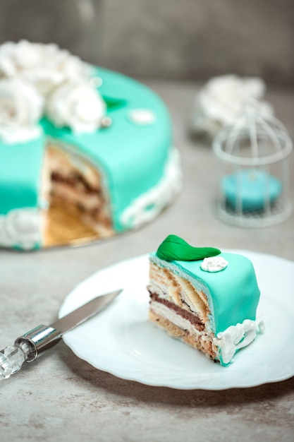 Plakje turquoise cake versierd met witte rozen en groene bladeren