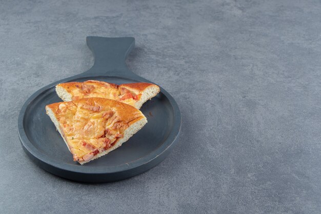 Plakjes gemengde pizza op zwarte snijplank.