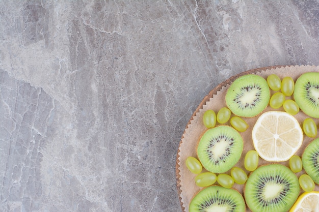 Plakjes kiwi, druiven en citroen op een houten bord.