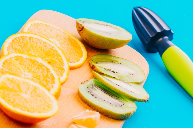 Plakjes sinaasappelen en kiwi plakjes en hand juicer op blauwe achtergrond