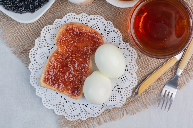 Plakjes vers wit brood met jam en gekookte eieren op marmeren achtergrond.