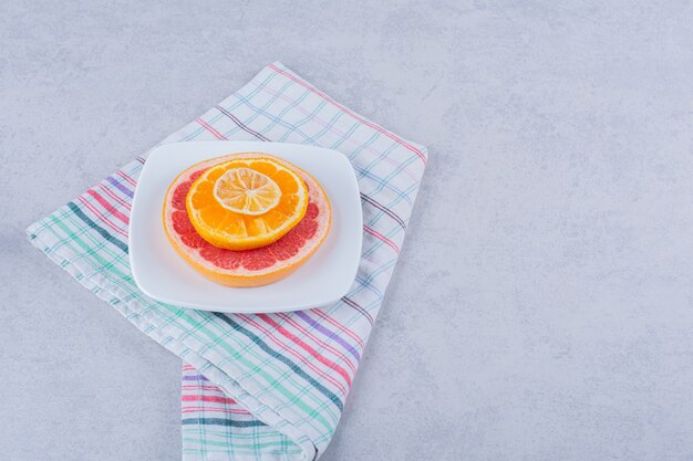 Plakjes verse grapefruit, sinaasappel en citroen op witte plaat.