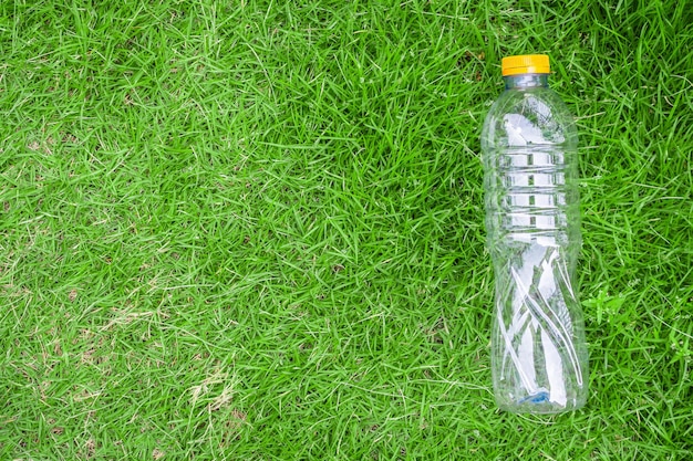 Plastic fles op groen gras als achtergrond recycle en vervuilingsconcept