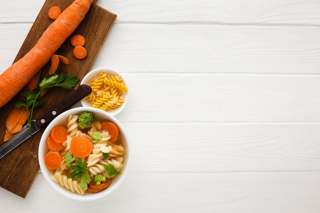 Gratis foto plat leg broccoli wortelen en fusilli in kom met wortel op snijplank met kopie ruimte