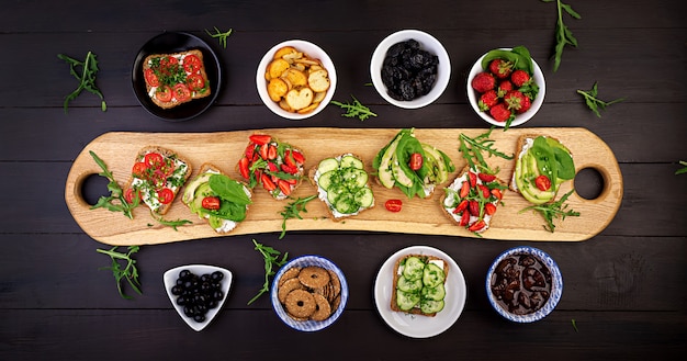 Gratis foto plat leggen van gezonde vegetarische tafel instelling. sandwiches met tomaat, komkommer, avocado, aardbei, kruiden en olijven, snacks. schoon eten, veganistisch eten