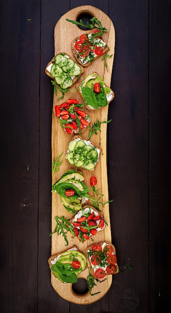 Plat leggen van gezonde vegetarische tafel instelling. sandwiches met tomaat, komkommer, avocado, aardbei, kruiden en olijven, snacks. schoon eten, veganistisch eten