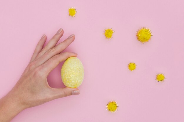 Plat leggen van hand met kleurrijke paasei met paardebloemen