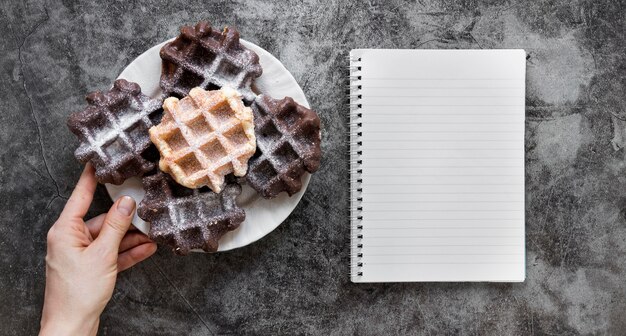 Plat leggen van hand met plaat van wafels en notebook