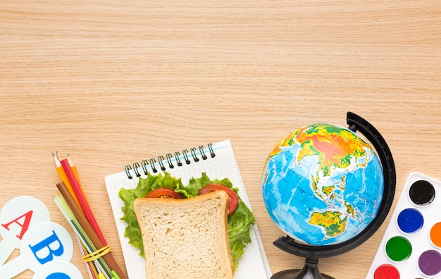 Plat leggen van schoolbenodigdheden met sandwich en globe