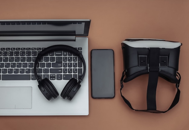 Platliggende samenstelling van moderne gadgets. laptop, vr-helm, koptelefoon, smartphone op bruine achtergrond. bovenaanzicht