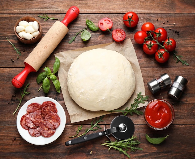 Gratis foto platte lay compositie met deeg en verse ingrediënten voor pepperoni pizza op houten tafel