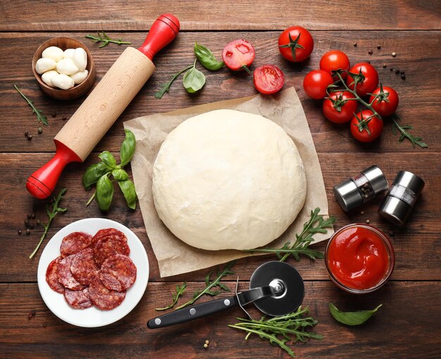 Platte lay compositie met deeg en verse ingrediënten voor pepperoni pizza op houten tafel