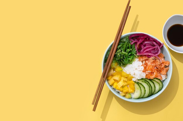 Poke bowl met rijst zalmkomkommermangoonionwakame salade maanzaad en zonnebloempitten geïsoleerd op gele achtergrondxA