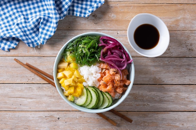 Poke bowl met rijstzalmkomkommermangoonionwakame salade maanzaad en zonnebloempitten op houten tafel