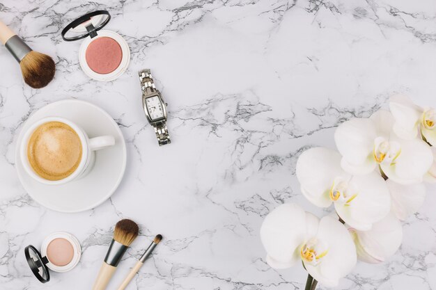 Polshorloge; koffiekop; compact poeder; make-up borstel en orchideebloem op marmeren achtergrond