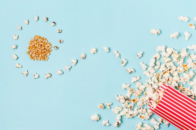 Gratis foto popcornzaden met gebogen popcorns gemorste voordoos op blauwe achtergrond