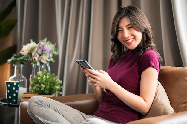 Portret aantrekkelijke slimme Aziatische vrouwelijke volwassen lang zwart haar casual glimlachend in de woonkamer op de bank met vrolijke frisheid en positieve emotie expressiondistance werken vanuit huis concept