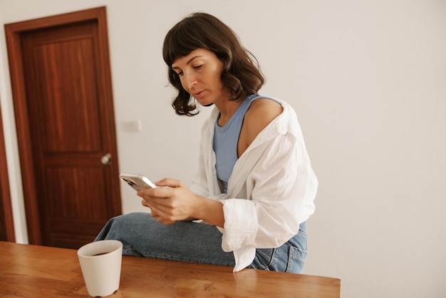 Portret blanke vrouw met koffie kijken naar telefoon