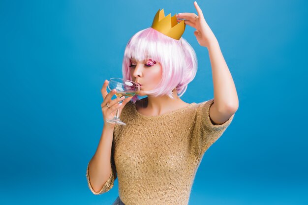 Portret blije jonge vrouw met roze kapsel champagne drinken met gesloten. Heldere make-up met roze tinsels, gelukkige viering, nieuwjaarsfeest, verjaardag.