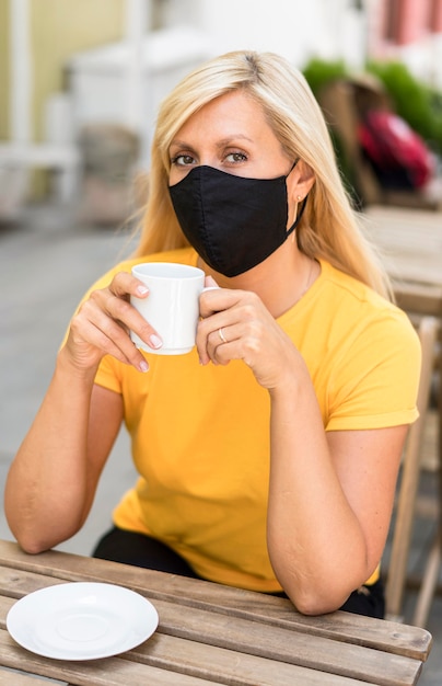 Gratis foto portret dat van vrouw stoffenmasker draagt dat een koffie houdt