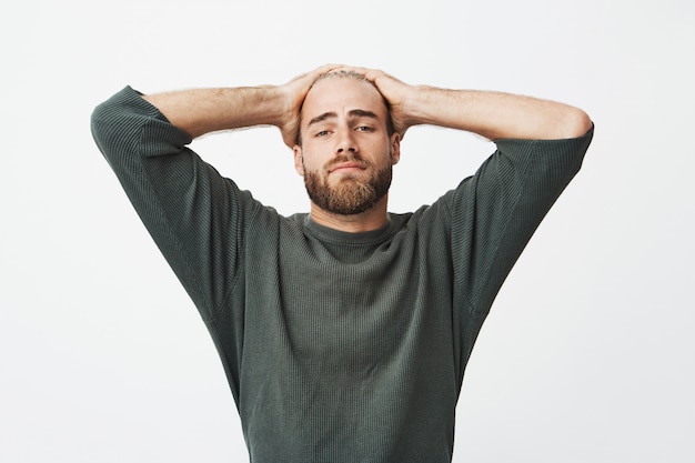 Portret die van de vermoeide knappe handen van de mensenholding op hoofd, terug op stoel leunen te rusten