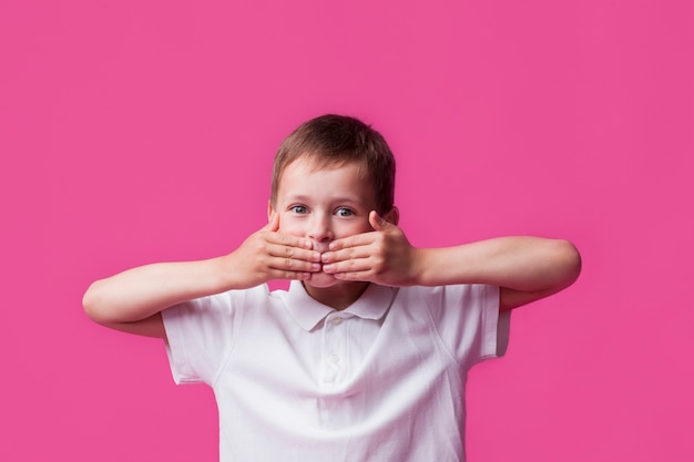 Portret die van onschuldige jongen zijn mond behandelen en camera over roze muurachtergrond bekijken