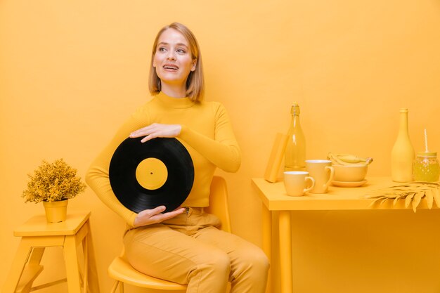 Portret die van vrouw een vinyl in een gele scène houden