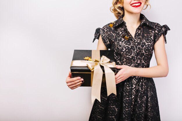 Portret gelukkige vrouw met zwarte geschenkdoos in de hand, rode lippen, zwarte jurk, glimlach.