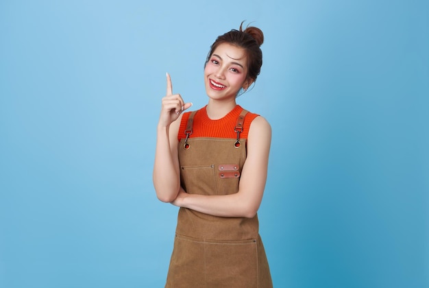 Portret jonge Aziatische barista vrouw met schort die staat en glimlacht en de vinger naar boven wijst