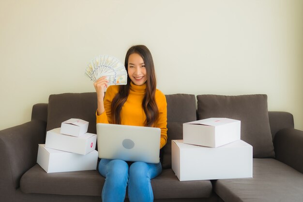 Portret jonge Aziatische vrouw die laptop computer voor het werk met pakketdoos met behulp van