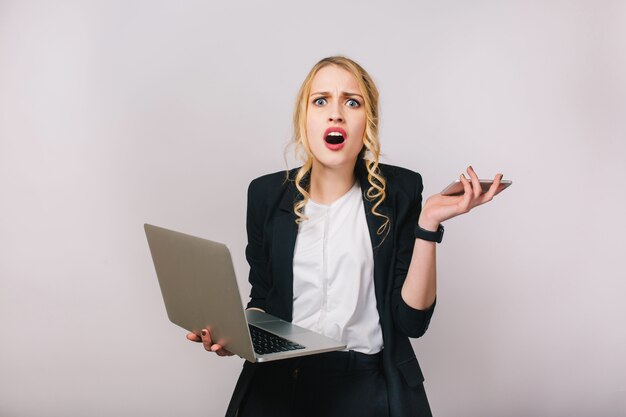Portret moderne mooie blonde kantoor vrouw in wit overhemd en zwarte jas. Werken met laptop, telefoon. verbaasd, overstuur, problemen, ware emoties uiten, druk bezig zijn