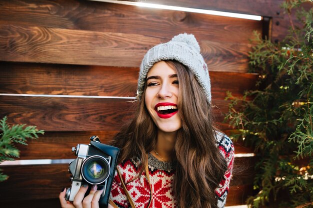 Portret mooi meisje met lang haar in gebreide muts met plezier met camera op houten.