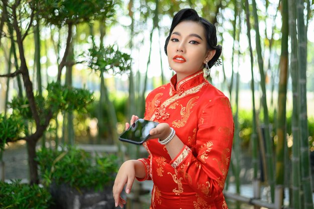Portret mooie Aziatische vrouw in een Chinese cheongsam poseren met smartphone op bamboebos
