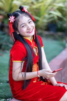 Portret mooie glimlach schattig klein aziatisch meisje met rode traditionele chinese cheongsam-decoratie die een selfie met smartphone neemt voor chinees nieuwjaarsfestival bij chinees heiligdom