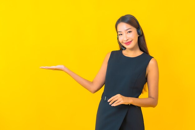 Portret mooie jonge Aziatische bedrijfsvrouw met de klantenzorg van het hoofdtelefooncall centre op gele achtergrond