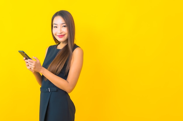 Portret mooie jonge Aziatische bedrijfsvrouw met koffiekop en slimme mobiele telefoon op gele achtergrond