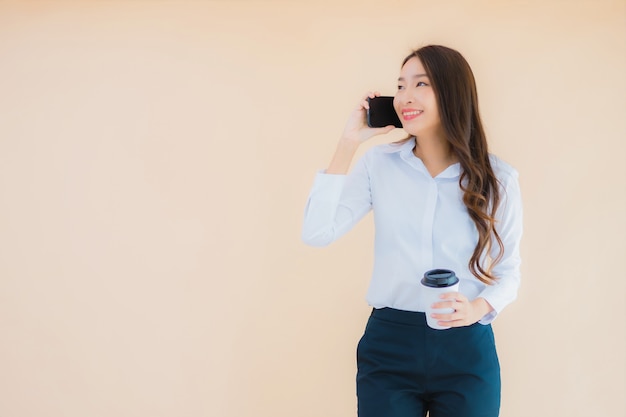 Portret mooie jonge Aziatische bedrijfsvrouw met slimme mobiele telefoon en koffiekop