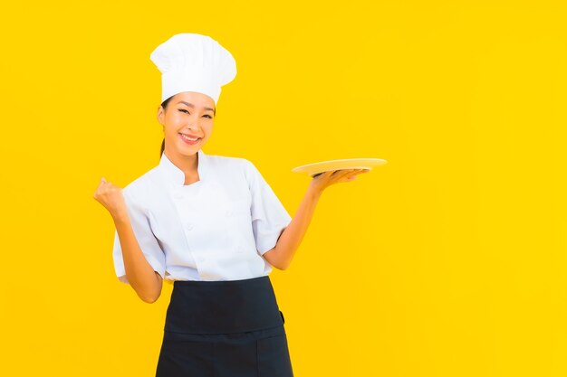 Portret mooie jonge Aziatische chef-kok vrouw met plaat op gele geïsoleerde background