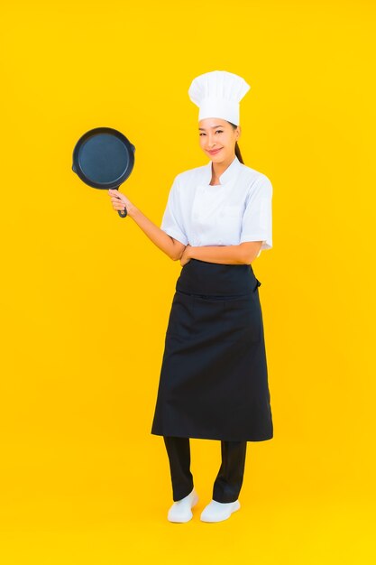 Portret mooie jonge Aziatische chef-kok vrouw met zwarte pan op gele geïsoleerde background