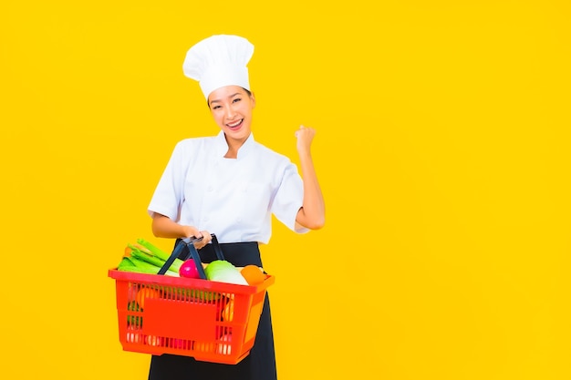 Portret mooie jonge aziatische chef-kokvrouw met kruidenierswinkelmand van supermarkt op gele geïsoleerde background