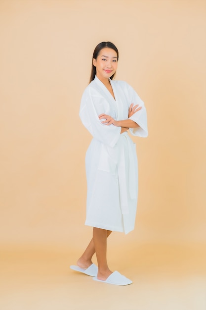Portret mooie jonge Aziatische vrouw die badjas met glimlach op beige draagt