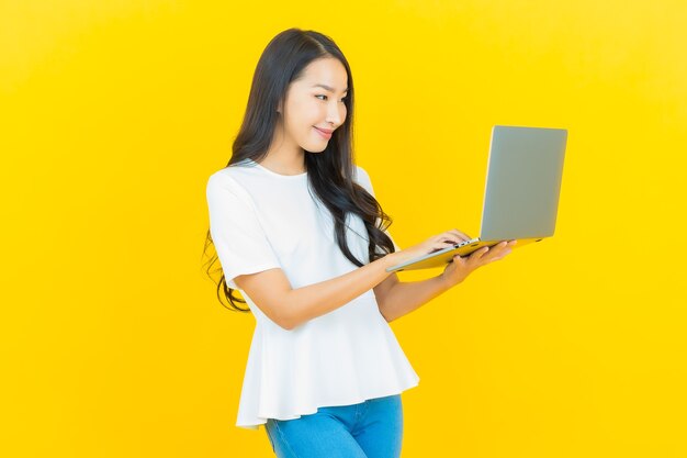 Portret mooie jonge Aziatische vrouw die lacht met computer laptop op geel on