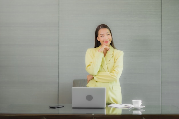 Portret mooie jonge Aziatische vrouw gebruik computer laptop met slimme mobiele telefoon op werktafel op interieur kamer