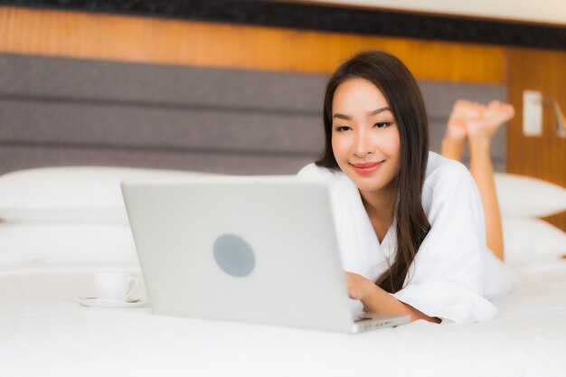 Portret mooie jonge Aziatische vrouw gebruik computer laptop op bed in slaapkamer interieur