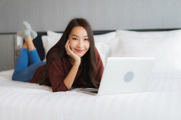 Portret mooie jonge Aziatische vrouw gebruik computer laptop op bed in slaapkamer interieur